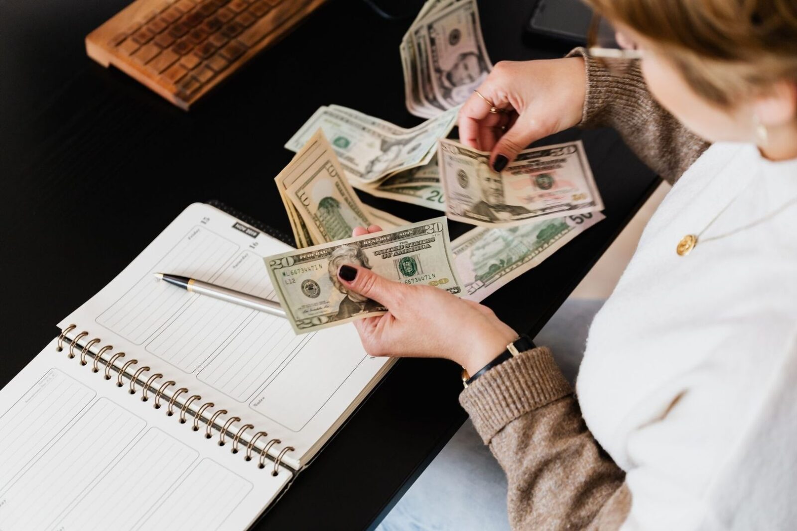 Person räknar amerikanska sedlar bredvid en öppen budgetbok