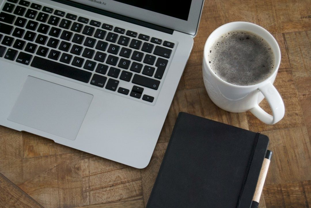 Laptop, kaffe och anteckningsbok på ett träbord för studentens planering